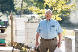 Buddy May amidst his many beehives on May Farms. The smoker in his hand is used to produce a kind of fire alarm in the hive, keeping the bees busy while May checks up on them.